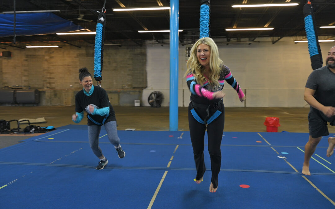 Two women and one man attached to bungee chords in a gym doing fitness