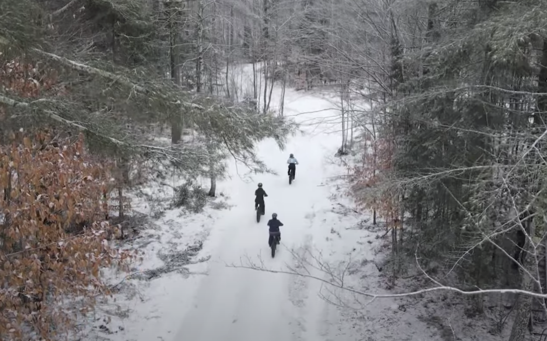 Three women riding bikes through a snow covered trail.