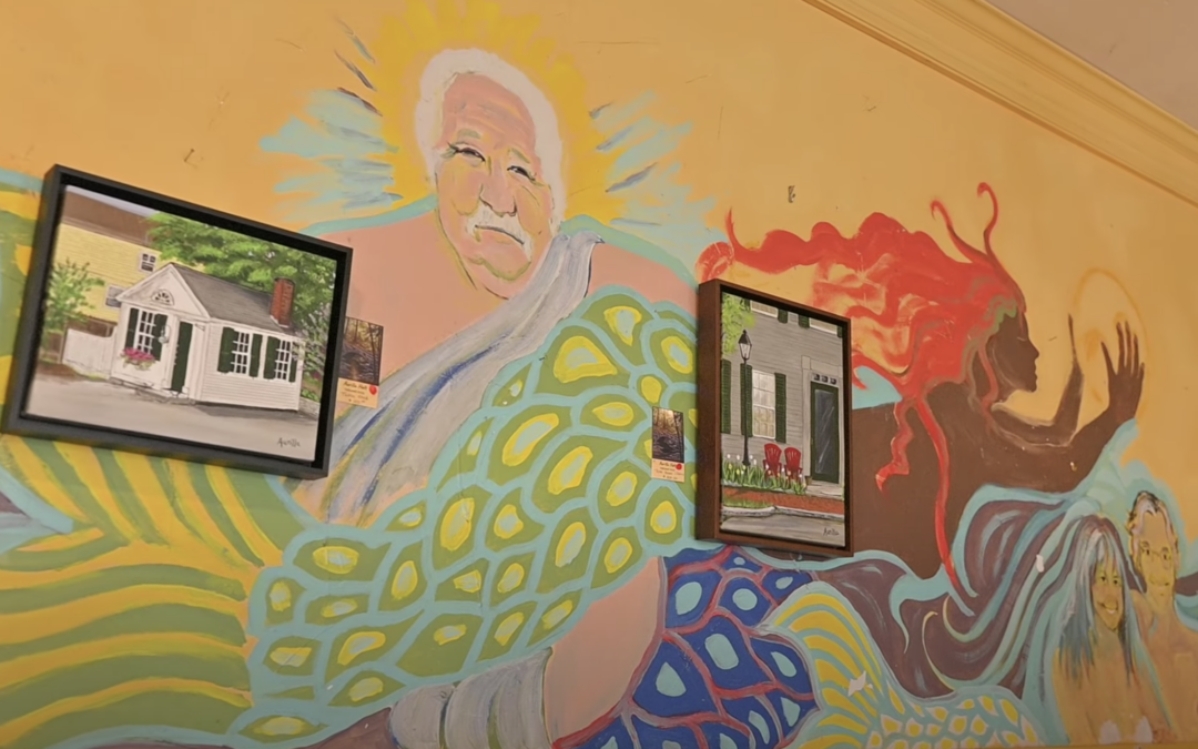 Colorful mural of a Merman holding two pictures which are hanging on the wall.