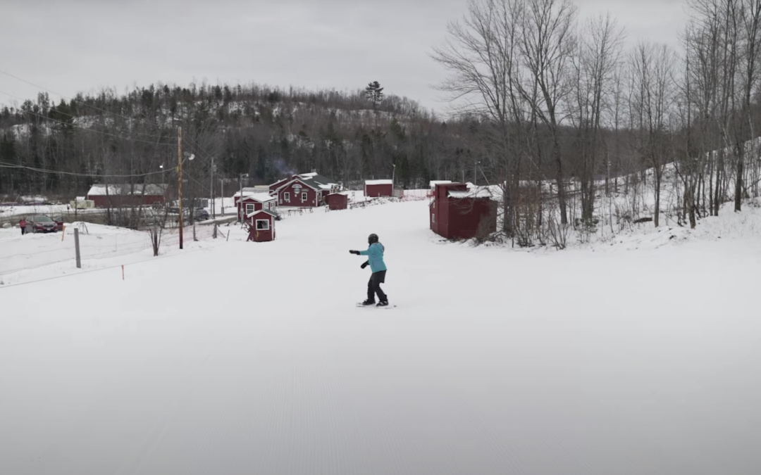 Woman snowboarding down slope towards red ski lodge