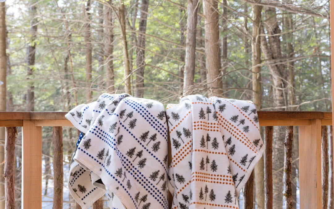 Blankets draped over a banister on a log cabin porch in the woods